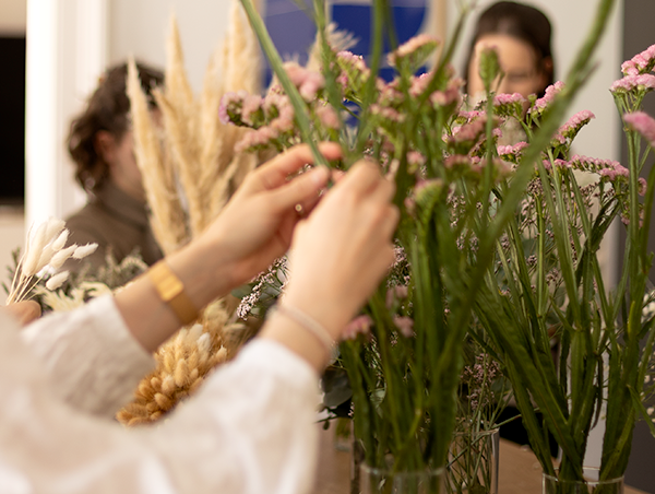 Teilnehmerin arrangiert zarte rosa Trockenblumen bei einem DIY-Workshop in Wien für das Binden von Blumenkränzen.
