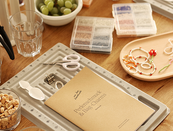Ein Arbeitstisch im we love handmade Studio für einen Perlenschmuck und Bag Charms Workshop mit Perlenbrettern, Zangen, bunten Perlenboxen, dem Workshop-Workbook und kleinen Snacks wie Nüssen und Weintrauben. | we love handmade