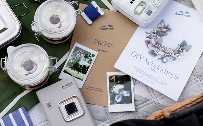 DIY-Workshops-Flyer von we love handmade neben Stick-Workbook, Stickgarn und Instax Kamera auf einer Picknickdecke